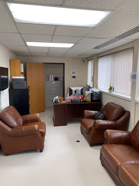 A small office lounge with leather chairs, a desk, and office equipment.