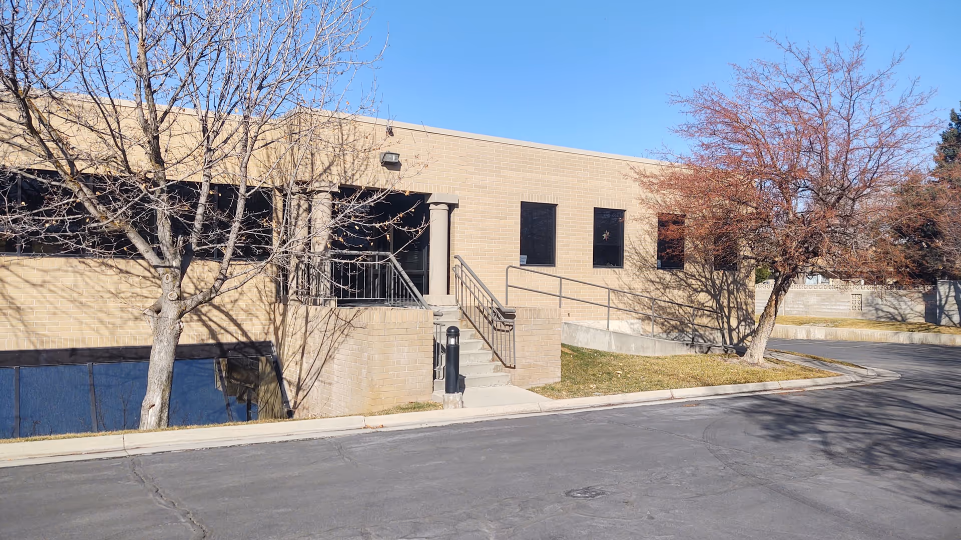 Exterior view of a brick facility with stairs, railings, and leafless trees.