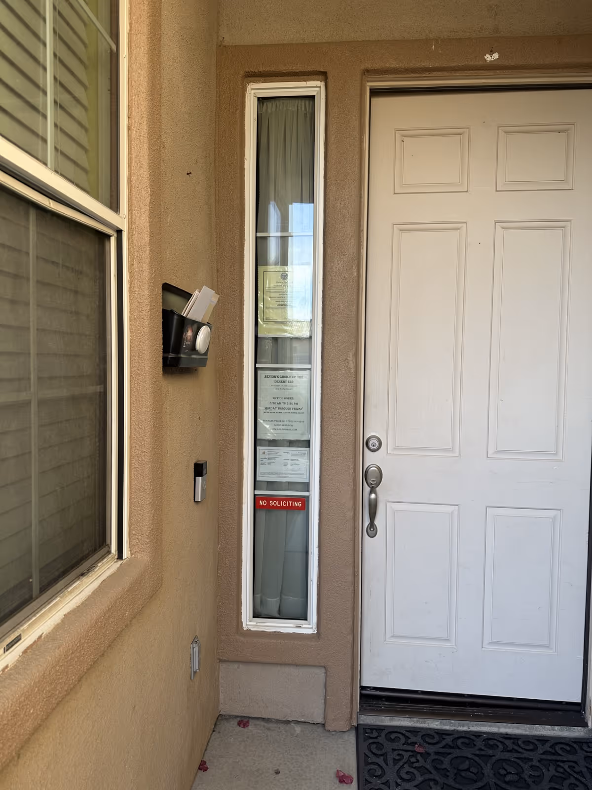 Front entrance of beige stucco building with a door, window, and posted notices.