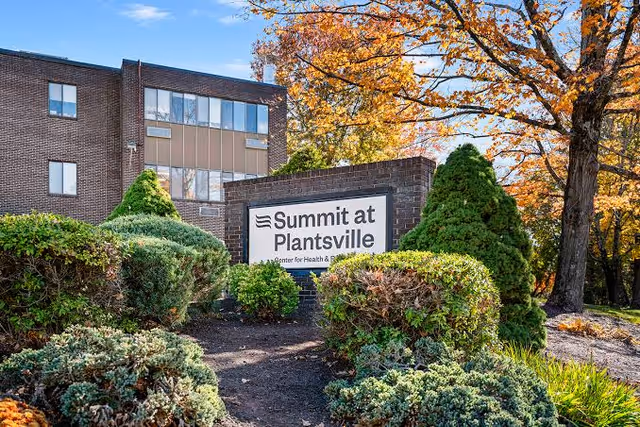 Exterior view of Summit at Plantsville entrance with landscaped bushes and sign.