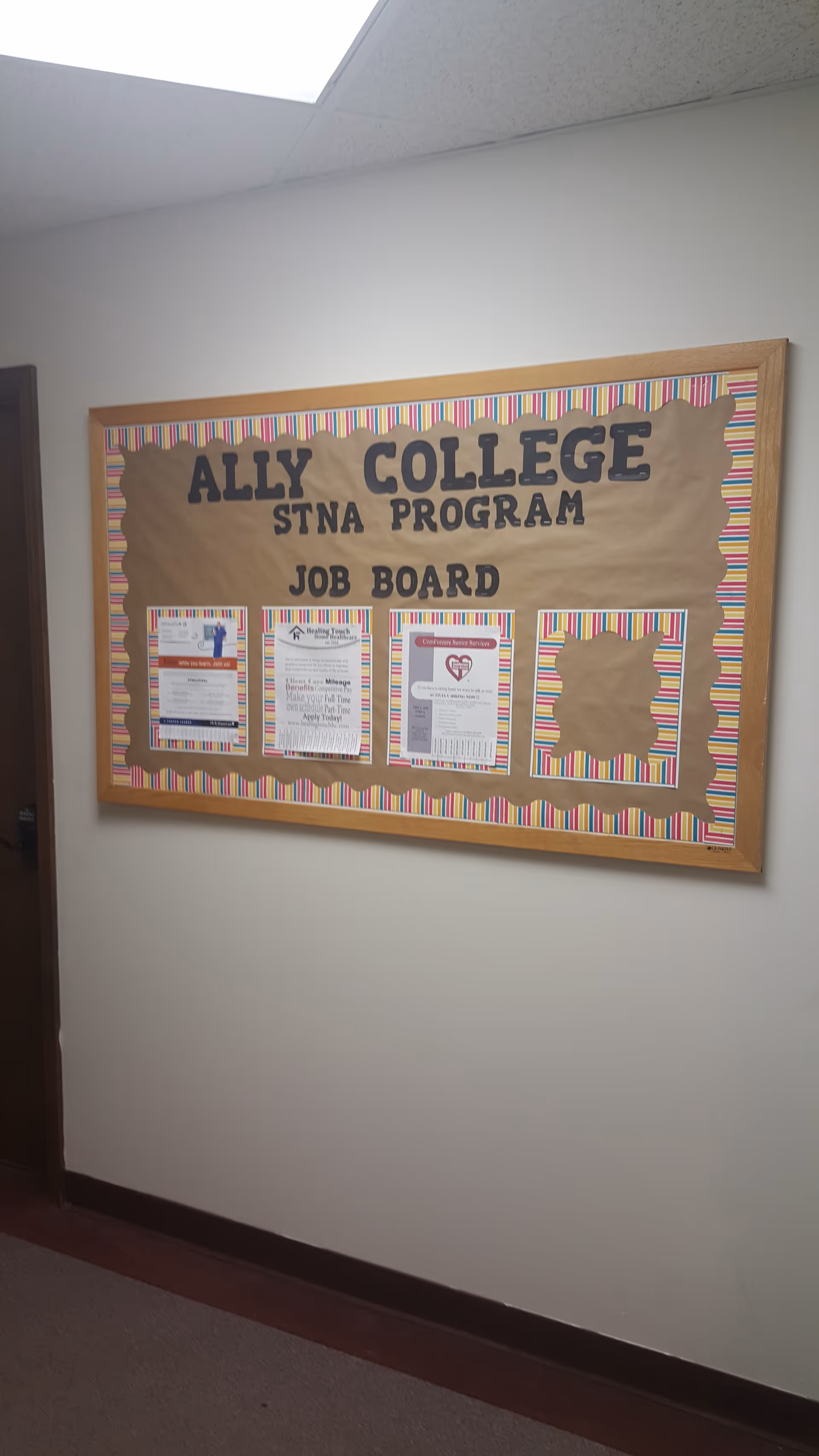 A hallway bulletin board labeled Ally College STNA Program Job Board on a beige wall.
