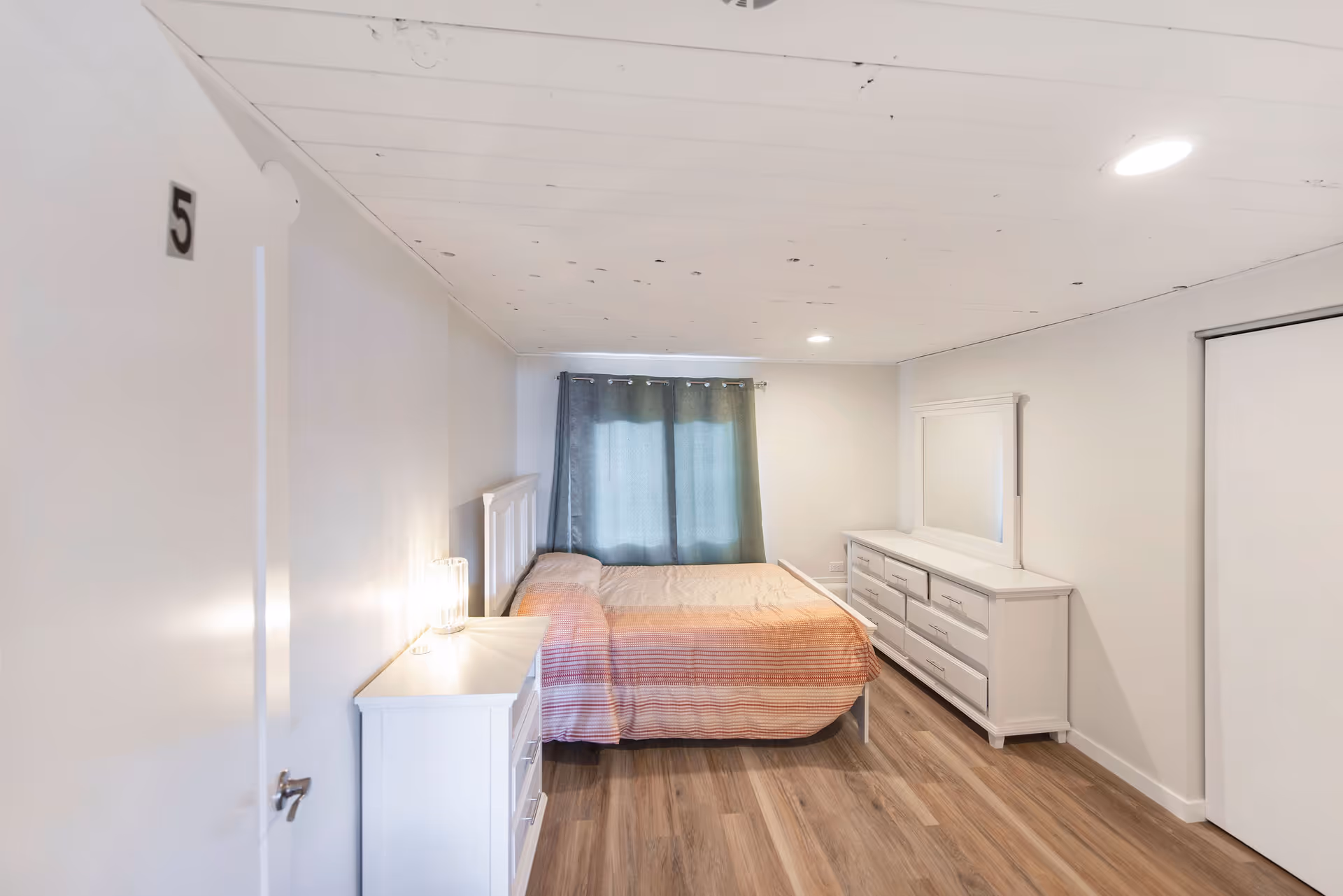 White-furnished bedroom with bed, dresser, nightstand, and window with curtains.