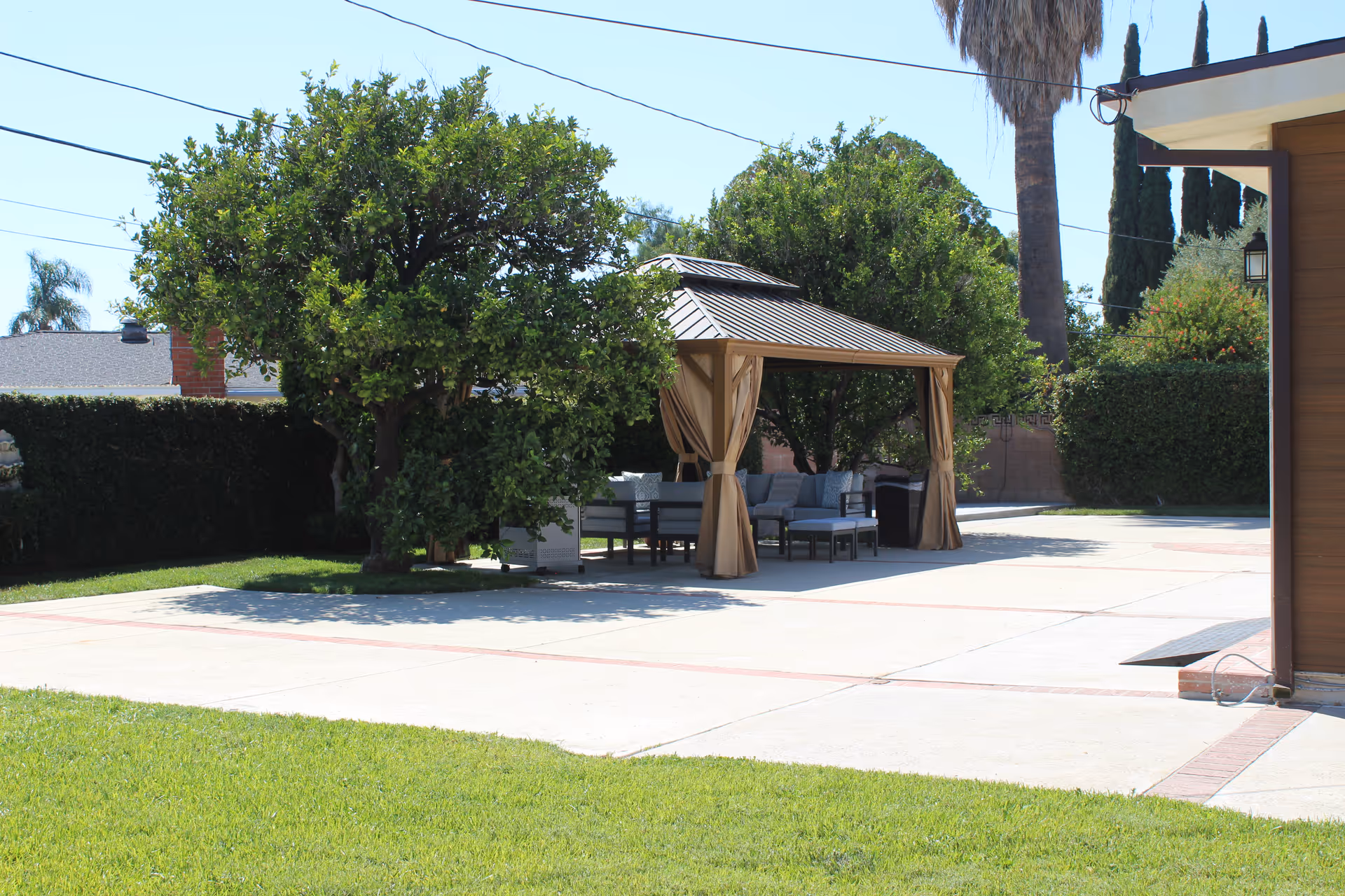 Outdoor patio with cushioned seating under a gazebo in a sunny yard.