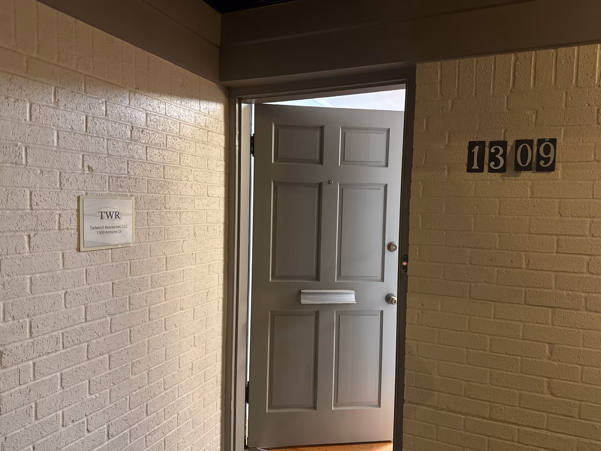 Interior hallway with a gray apartment door labeled 1309 and a plaque on brick wall.