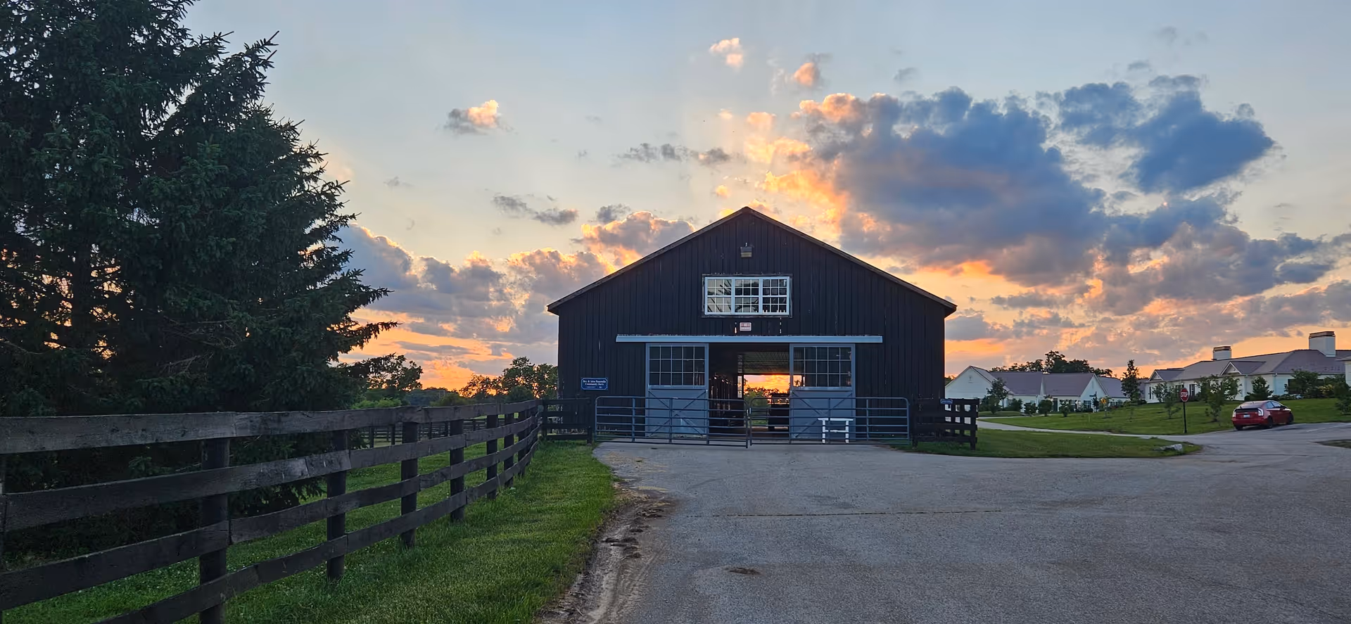 Sunset-lit exterior of a barn-style senior living facility with a fence and road.