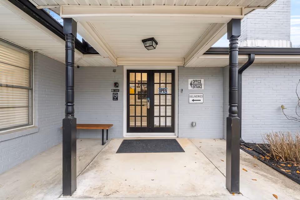 Covered entrance to a senior living facility with glass doors and a bench.