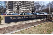 Front view of The Leah Rose Residence sign with parked cars and a multi-story building.