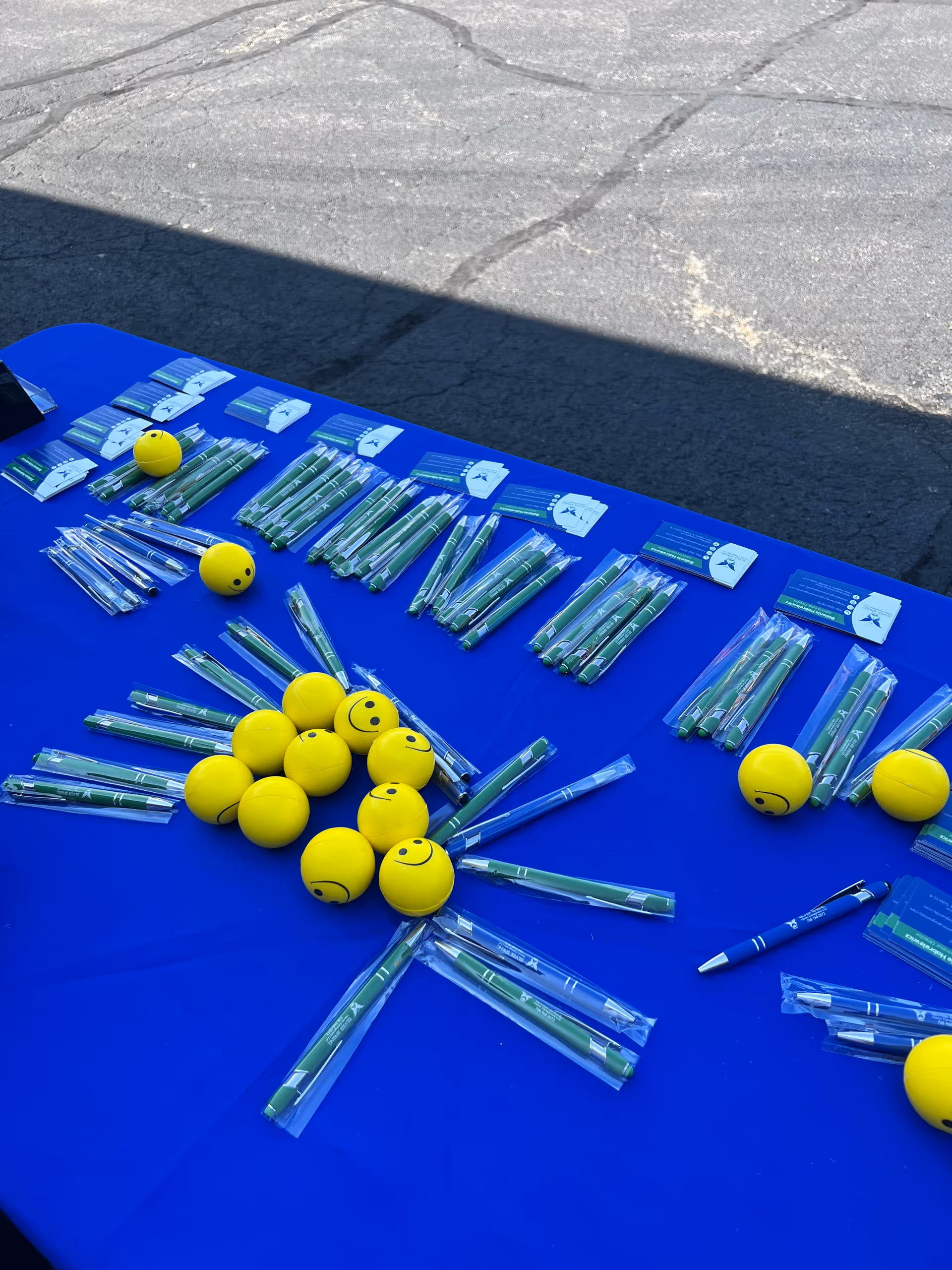 Blue outdoor table with pens, cards, and yellow smiley balls arranged.