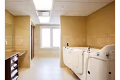 Laundry room with washers and dryers along beige tiled walls and a back window.