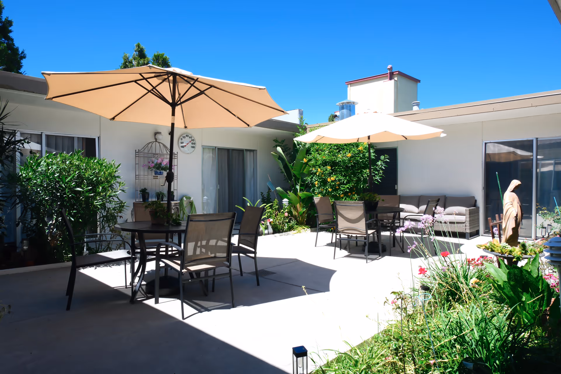Outdoor courtyard with patio tables, chairs, and umbrellas surrounded by plants.