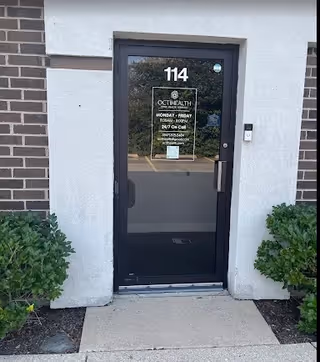 Front entrance of Octihealth Home Health Agency building at 114 with glass door and greenery.