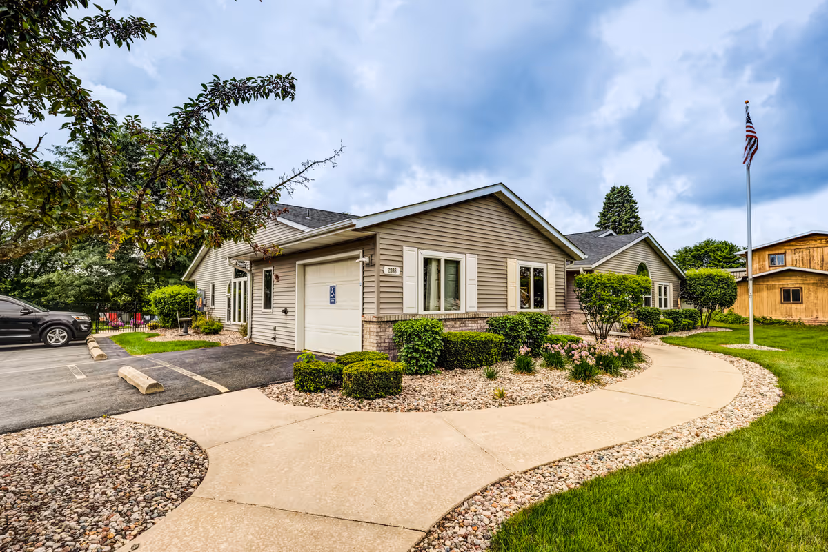 Curved walkway leads to a single-story senior living facility with landscaped front.