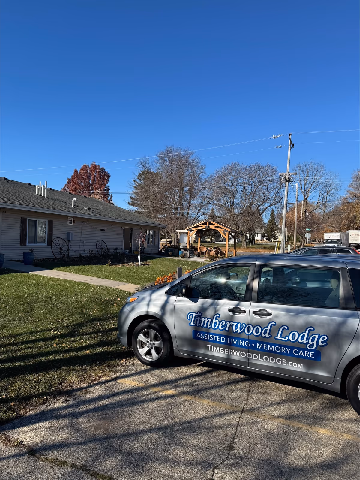 Exterior view of a single-story senior living facility with a Timberwood Lodge van and gazebo.