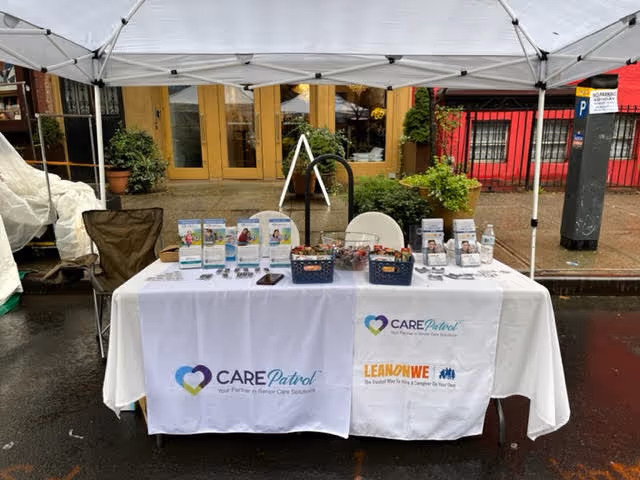 Outdoor promotional table under a white canopy displaying LeanOnWe Home Care brochures and CAREPatrol materials.