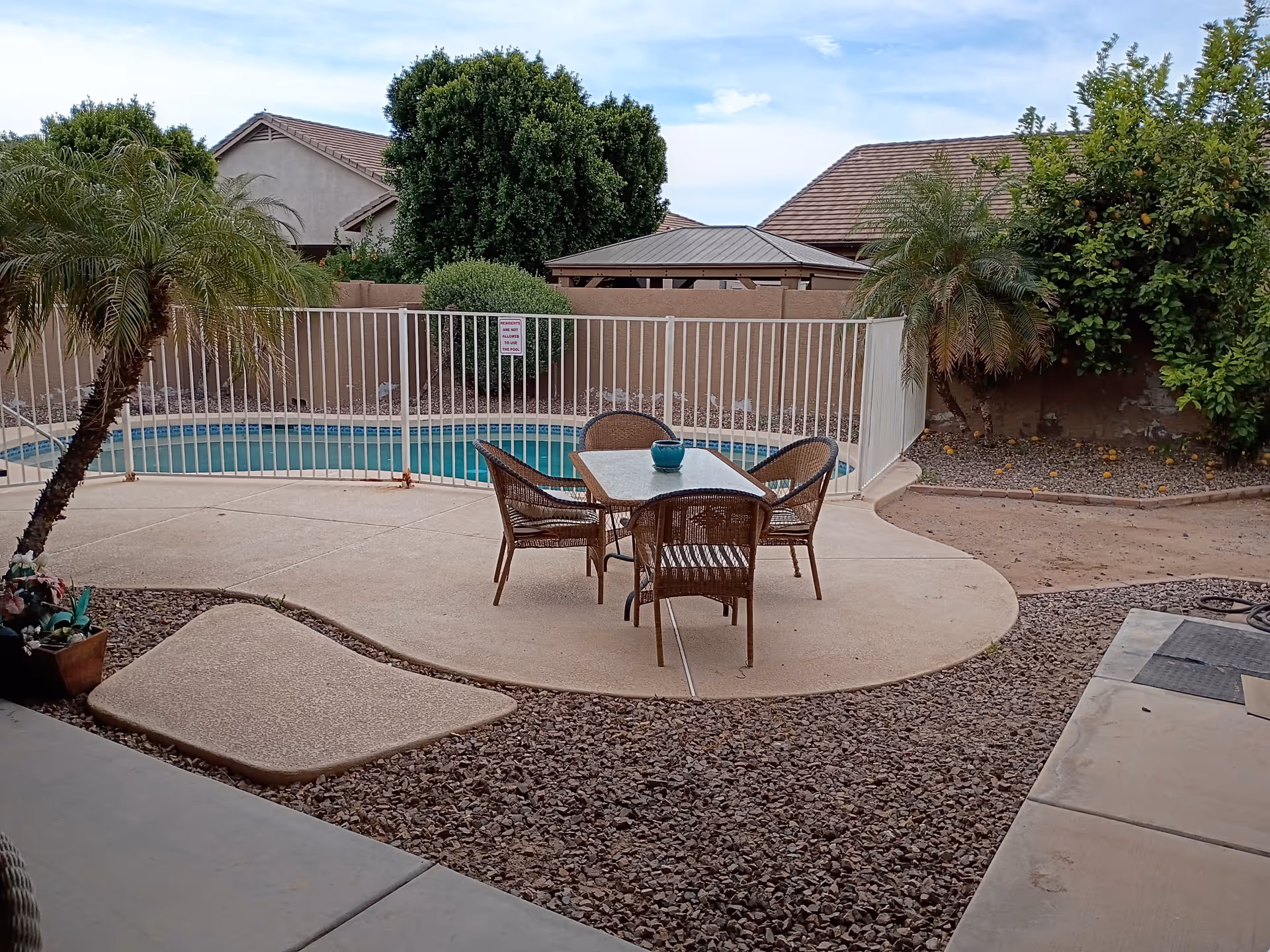 Outdoor patio area with a table and chairs beside a fenced swimming pool.