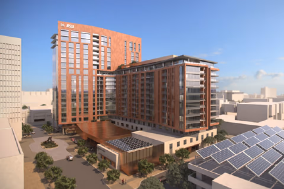 Rendered exterior view of a multi-story modern senior living building with a driveway and solar panels on a nearby rooftop.