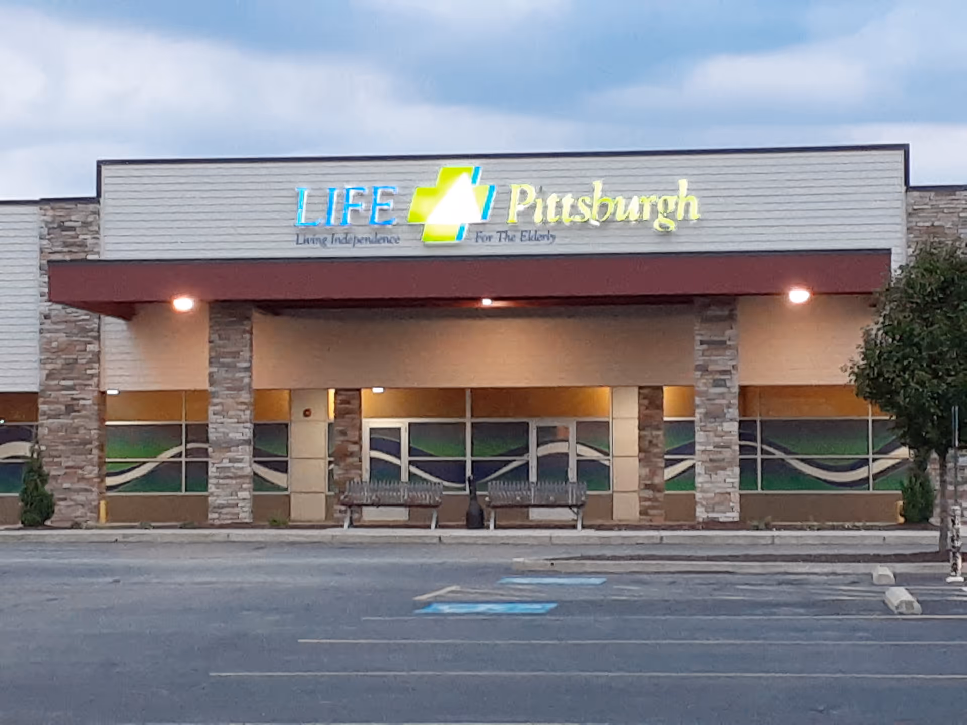 Exterior view of LIFE Pittsburgh McKees Rocks Day Health Center entrance with sign and benches.