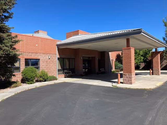 Brick senior living facility exterior with a covered entrance and parking under blue sky.