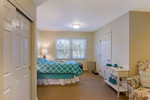 Bedroom in a senior living facility with teal patterned bedspread and window view