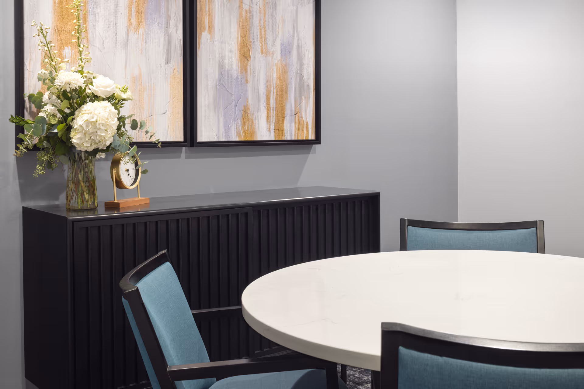 Interior dining area with round white table, blue chairs, and abstract art.