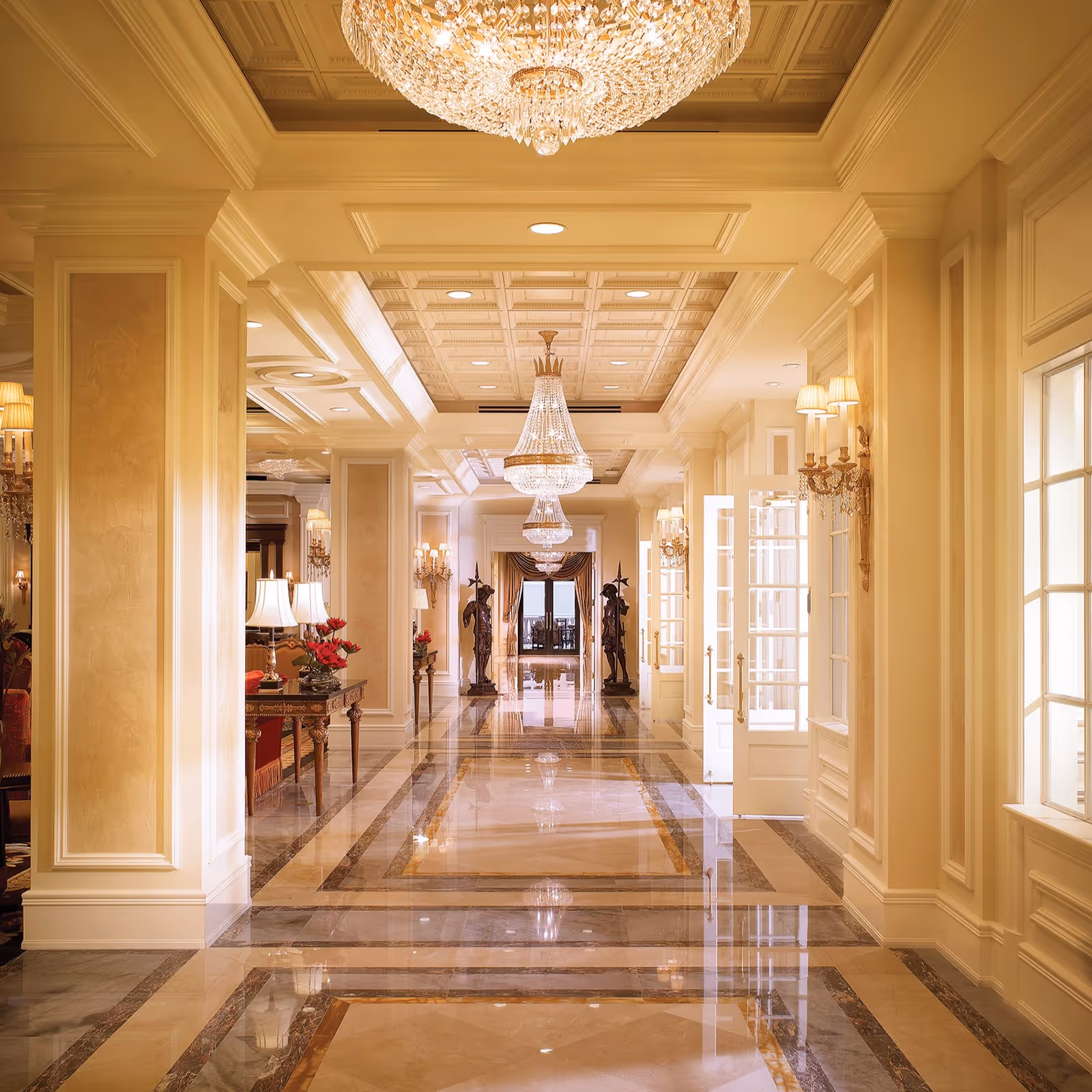 Elegant hotel-like hallway with chandeliers, marble floors, and ornate walls in a senior living facility.