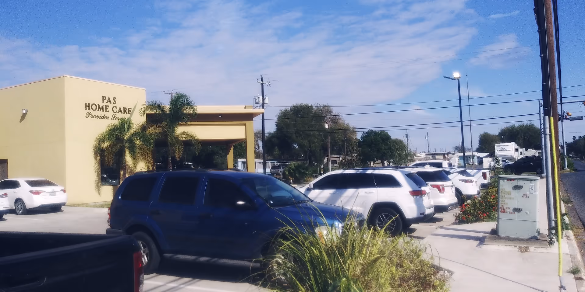 Front view of Pas Home Care building with palm trees, parked cars, and blue sky