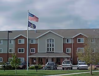 Front view of Plaza North Senior Residences with flagpoles and parked cars.