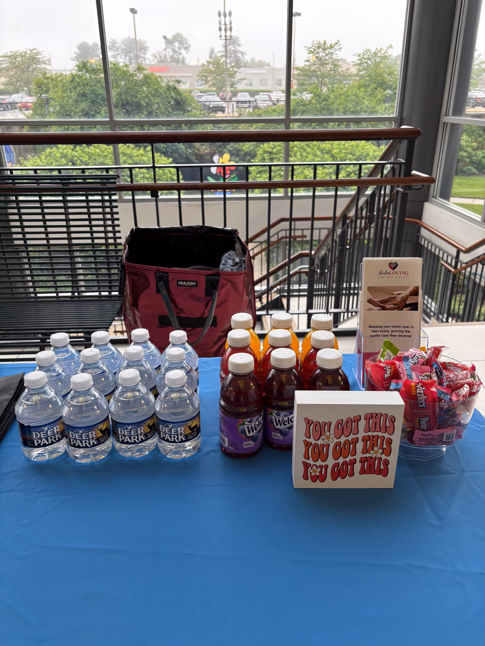 Indoor table setup with water bottles, juice, snacks, and a tote bag.