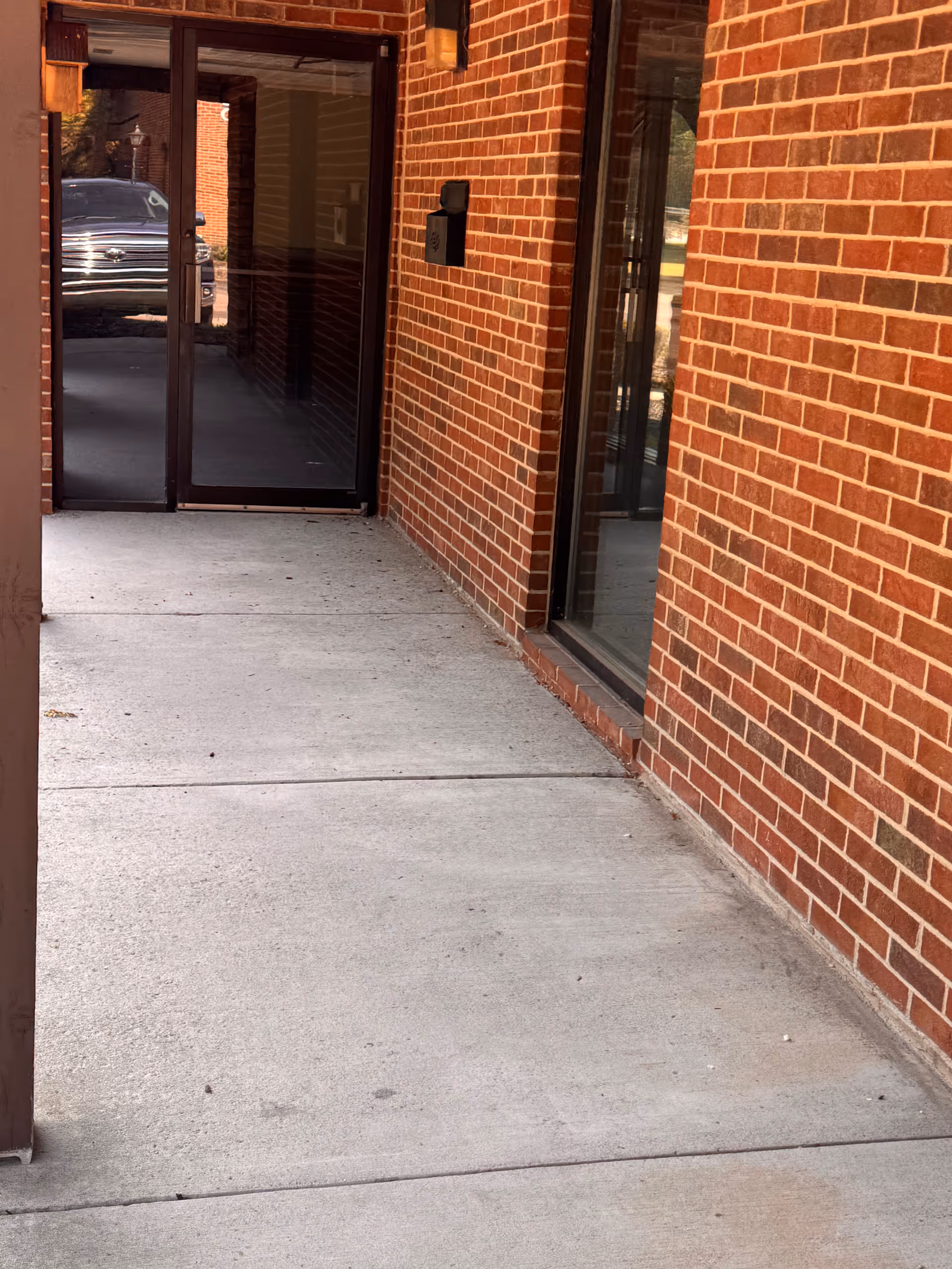 Brick exterior corridor leading to glass entrance of senior care facility.
