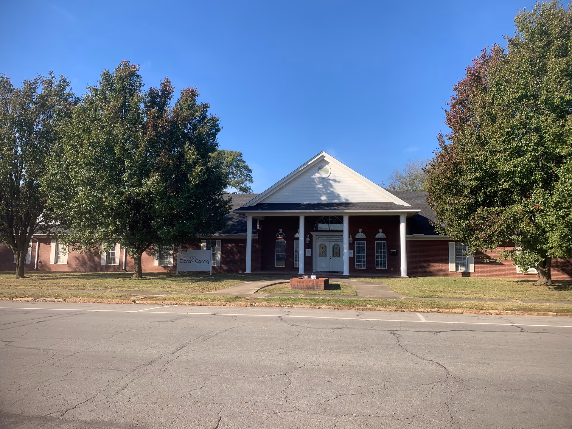 Elara Caring facility exterior with brick walls, white columns, and a clear sky.