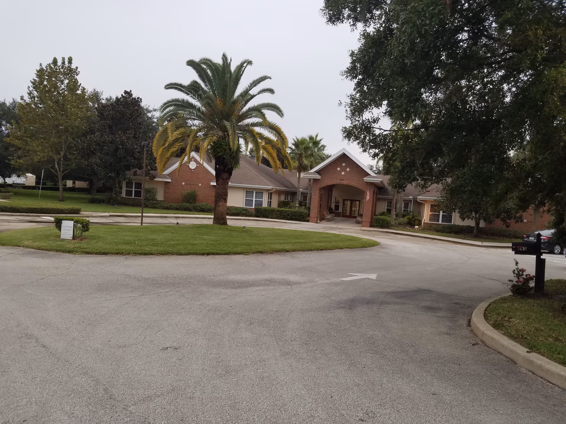 Brick senior living facility entrance with palm trees and circular driveway.