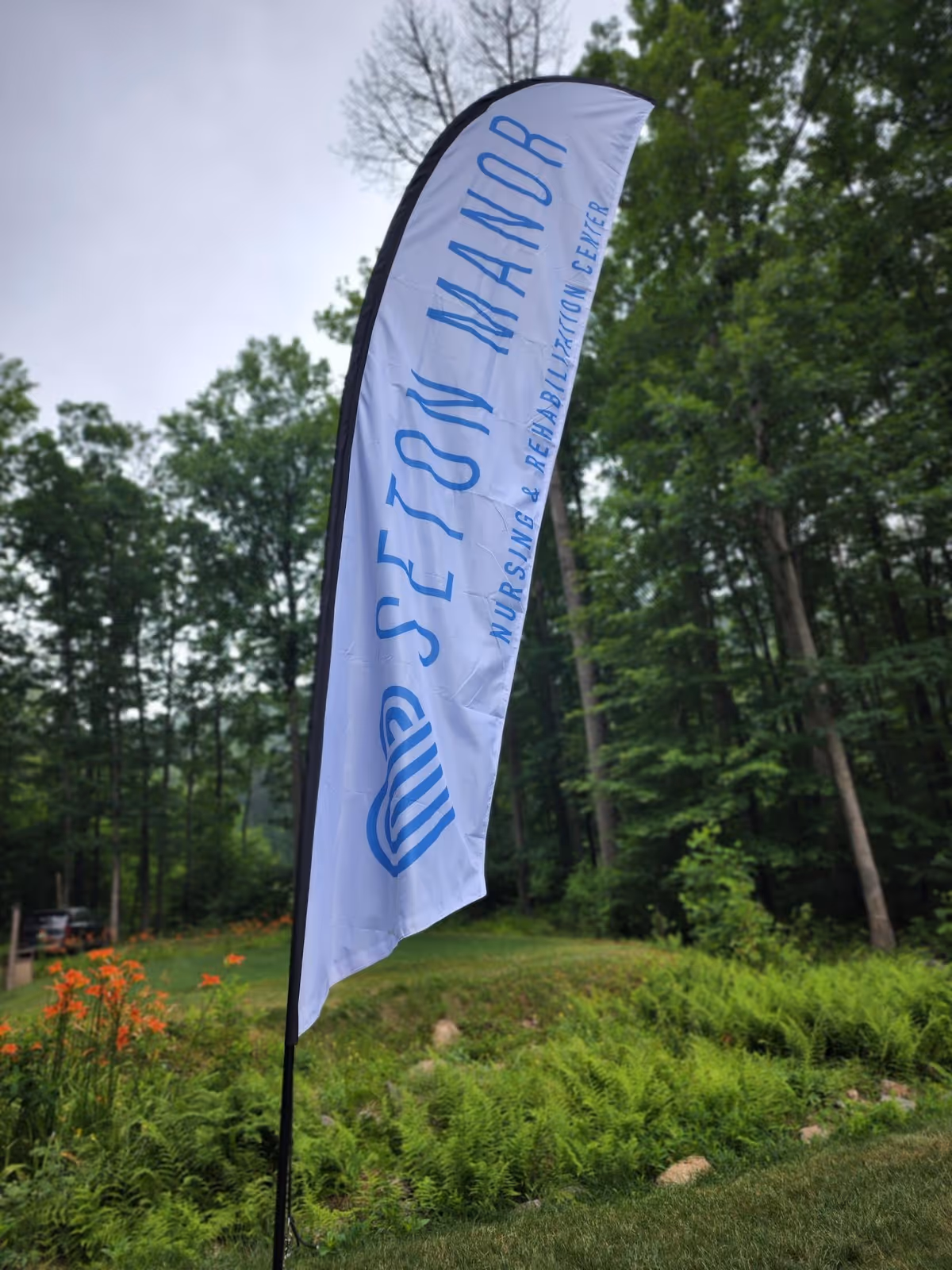 White vertical banner reading Seton Manor Nursing and Rehabilitation Center outdoors amid trees.
