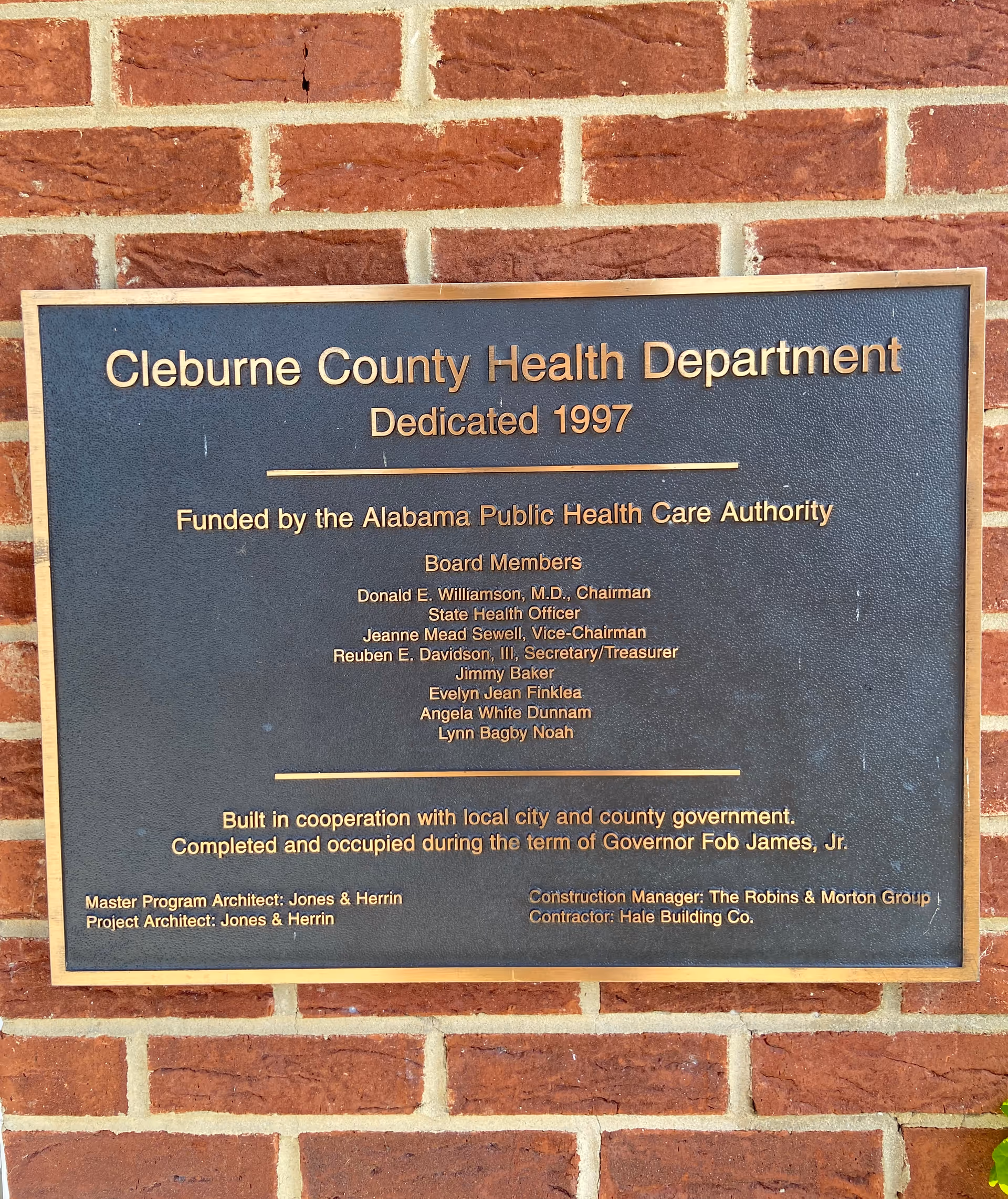 Bronze plaque mounted on a red brick wall reading Cleburne County Health Department.
