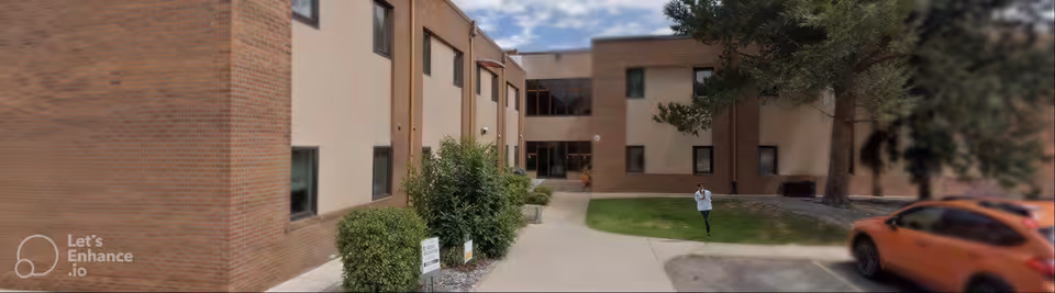 Exterior view of a brick senior living facility with a walkway, greenery, and a person walking.