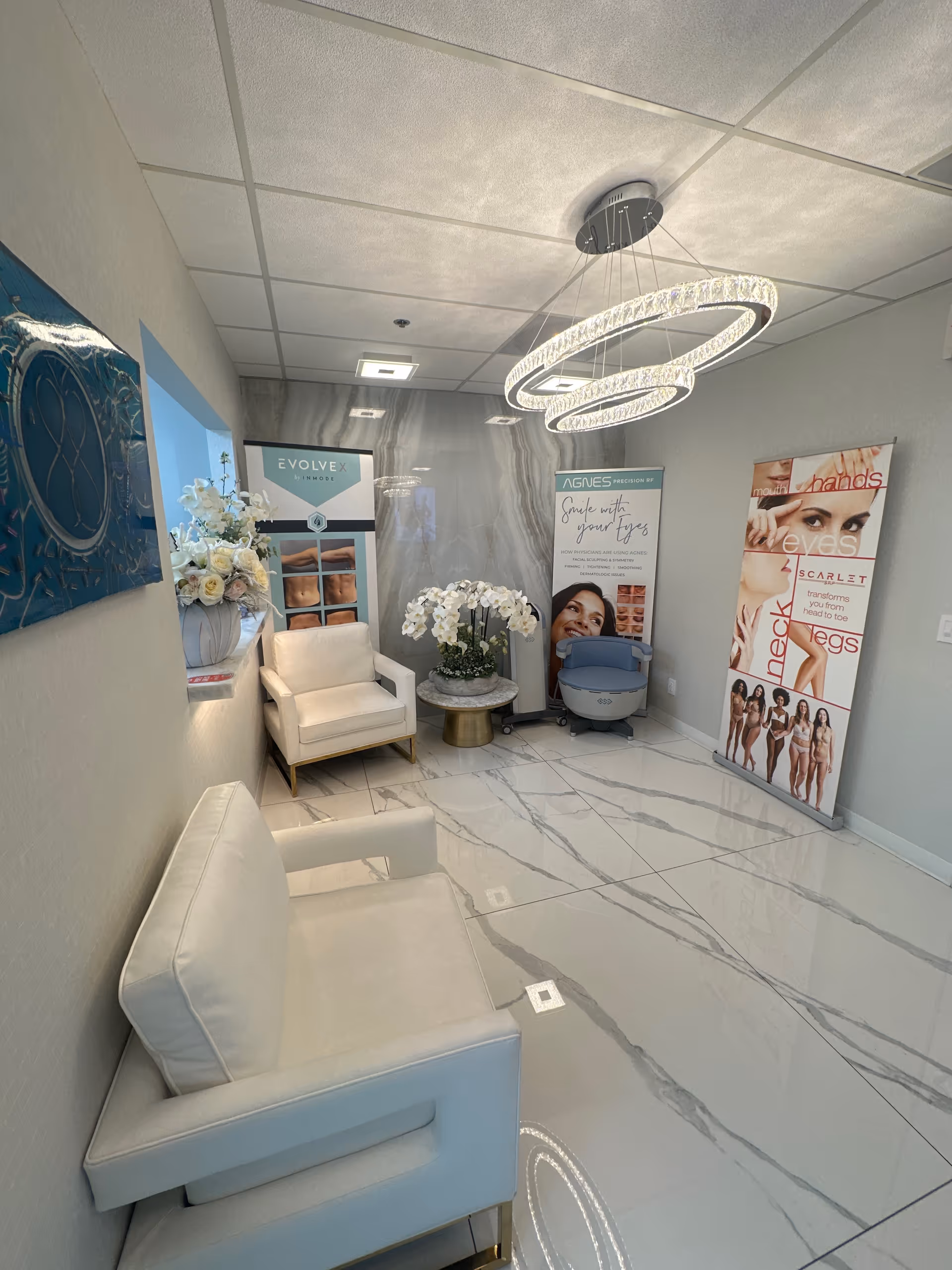 Modern waiting area with white seating, marble floors, and circular chandelier.