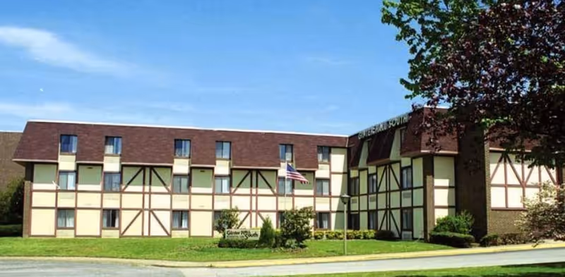 Three-story Tudor-style building facade with a lawn, an American flag, and a sign for Ginter Hall South.
