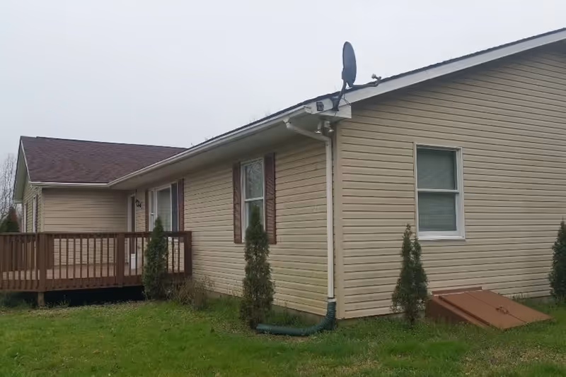 Exterior view of a beige, single-story building with a wooden deck and satellite dish.