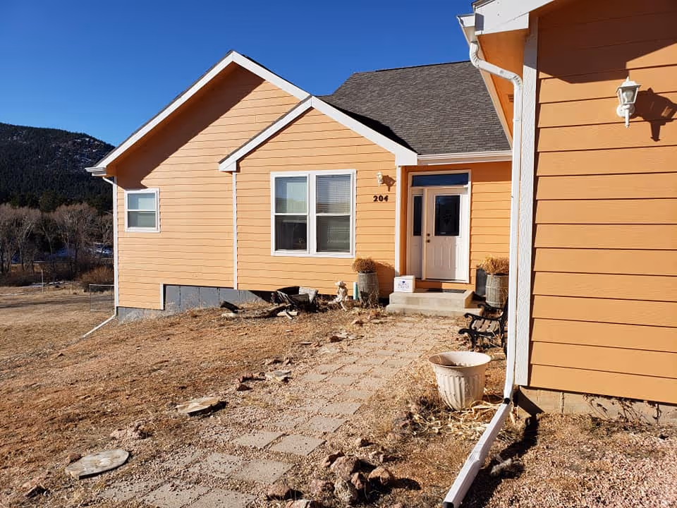 Orange siding senior living facility exterior with front entrance and gravel pathway.