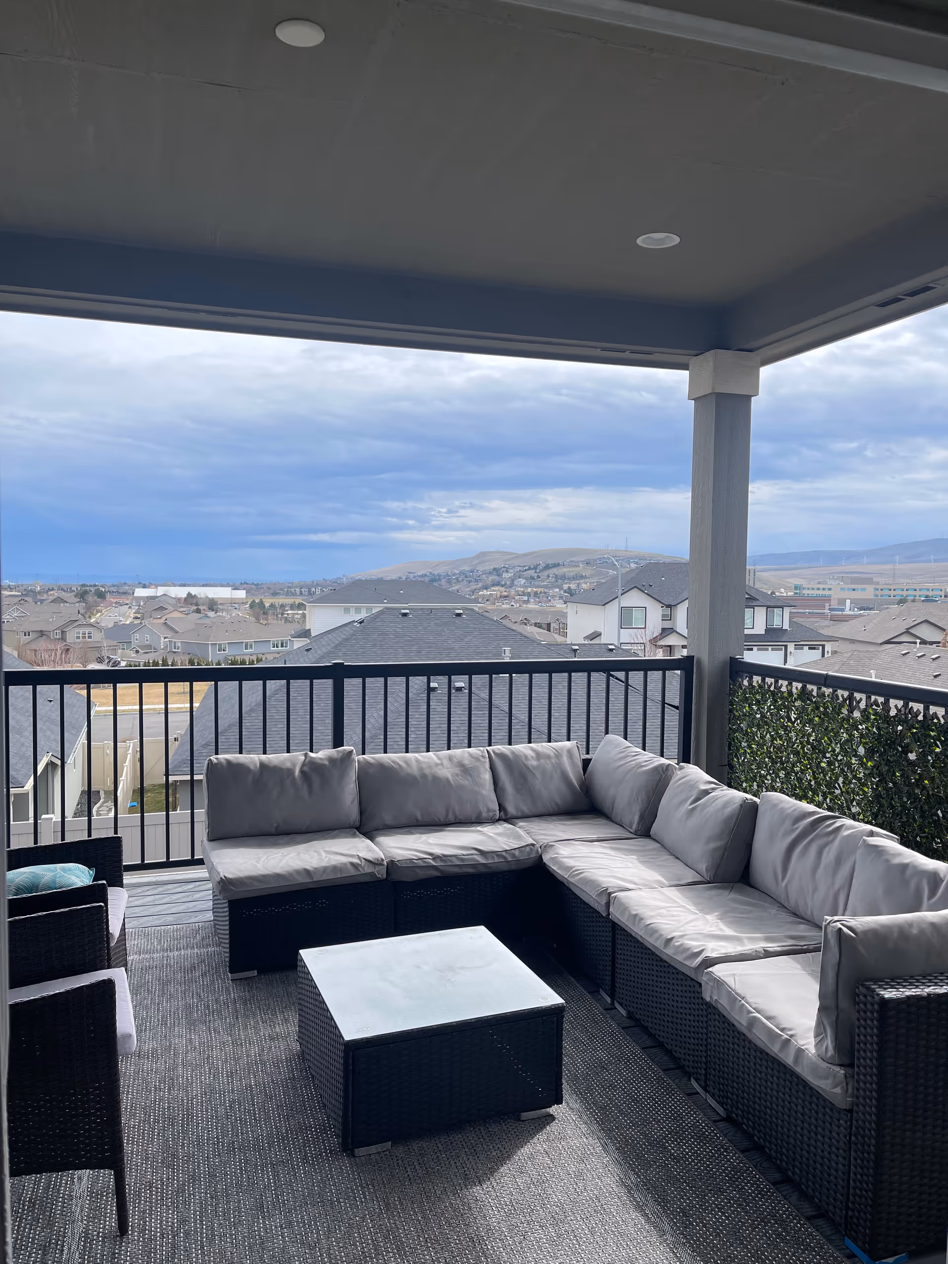 Outdoor balcony seating on a covered deck with a gray wicker sectional and view of rooftops