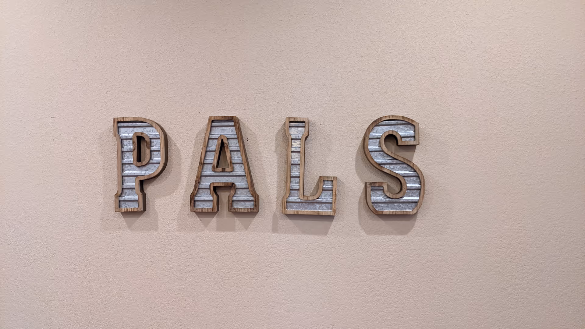 Interior wall with large metal letters spelling PALS mounted on beige surface