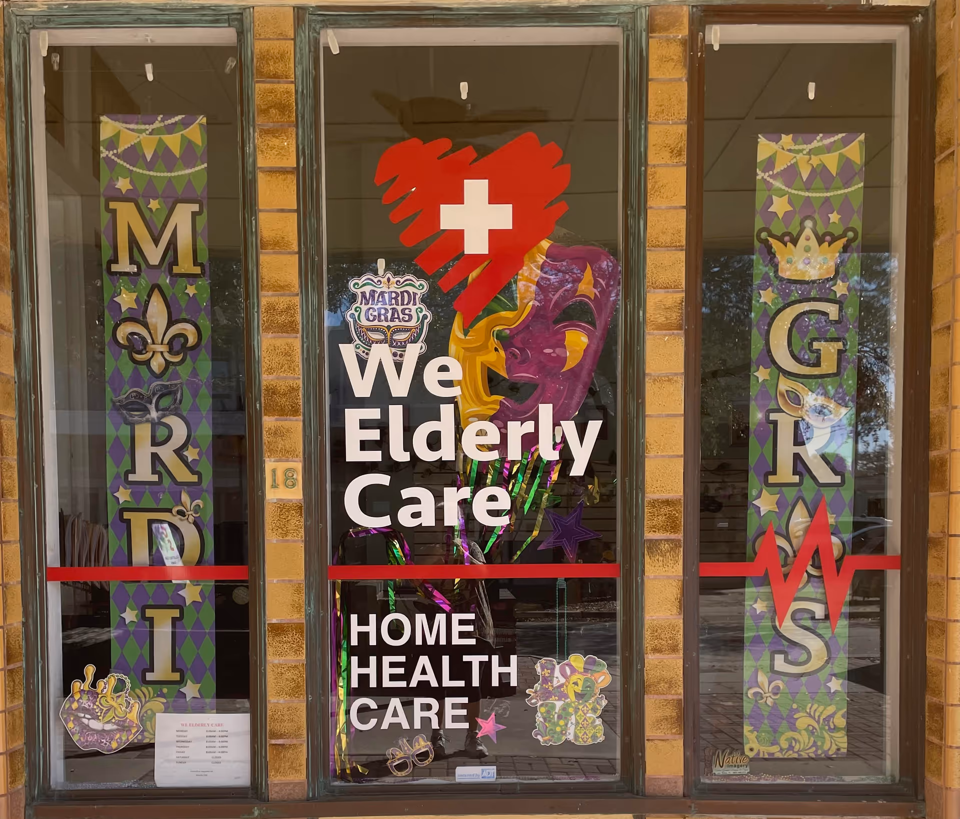 Storefront windows display We Elderly Care sign with Mardi Gras decorations.