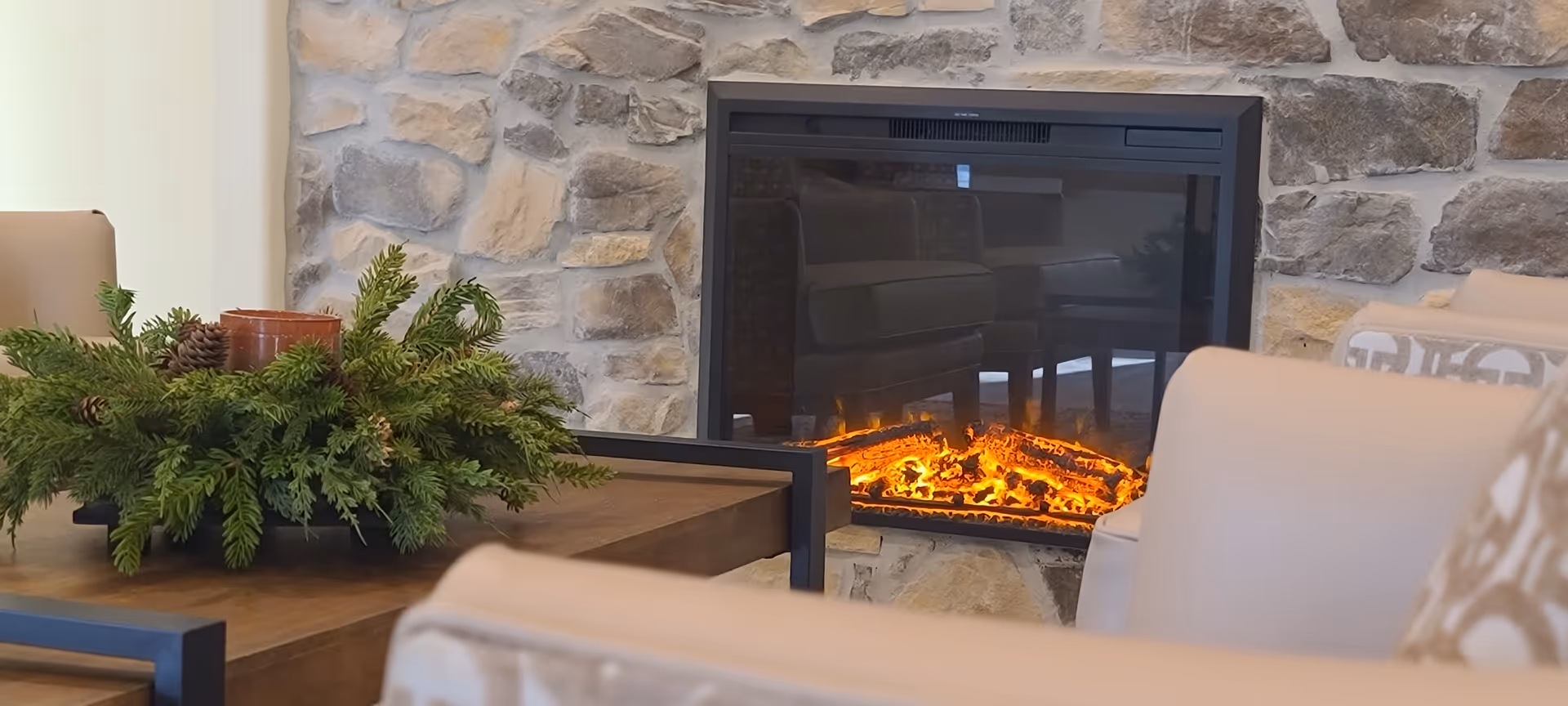 Stone fireplace with glowing fire, flanked by chairs and a wooden coffee table.
