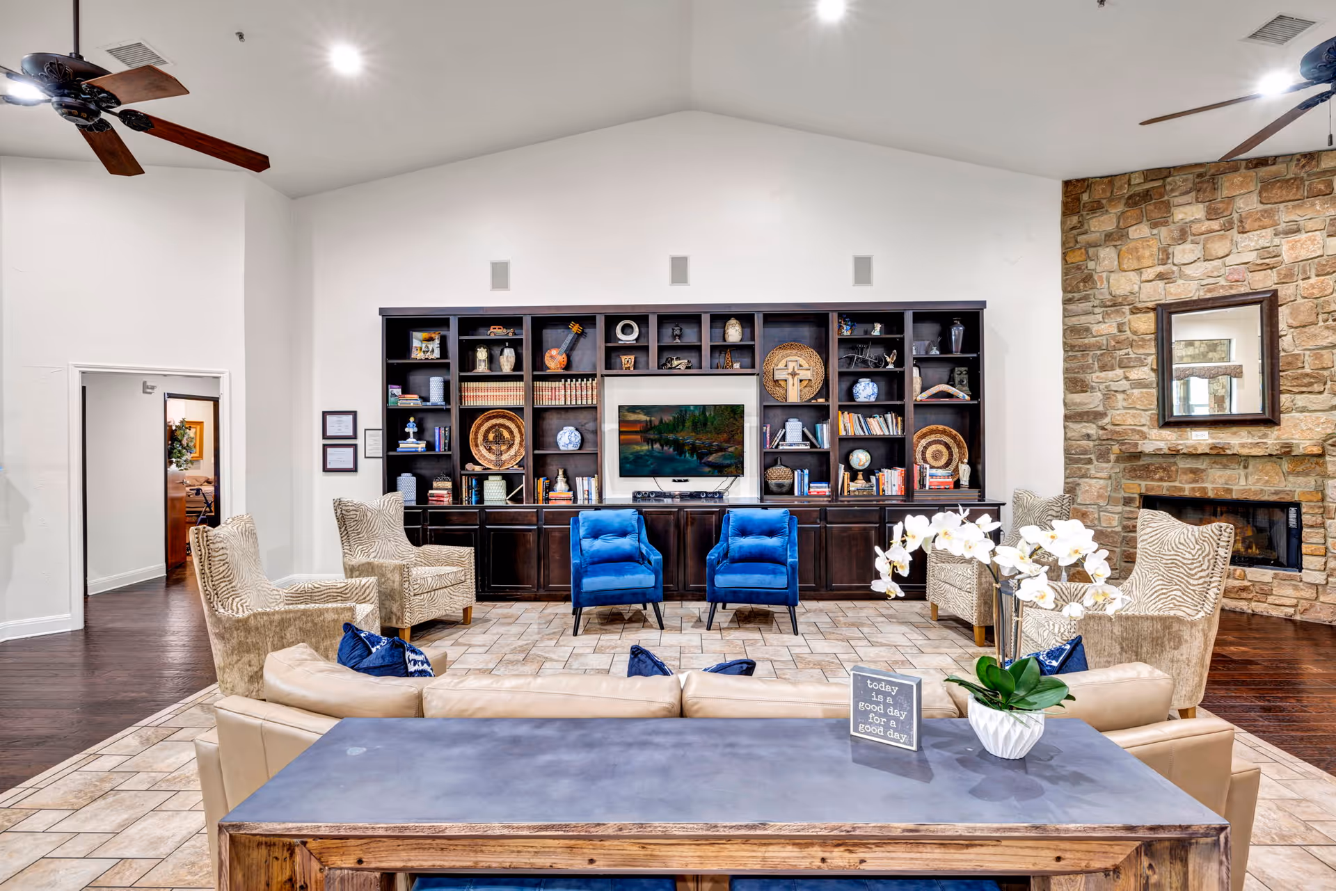 Spacious Arbor House lounge with blue chairs, beige seating, a bookcase wall, and a stone fireplace.