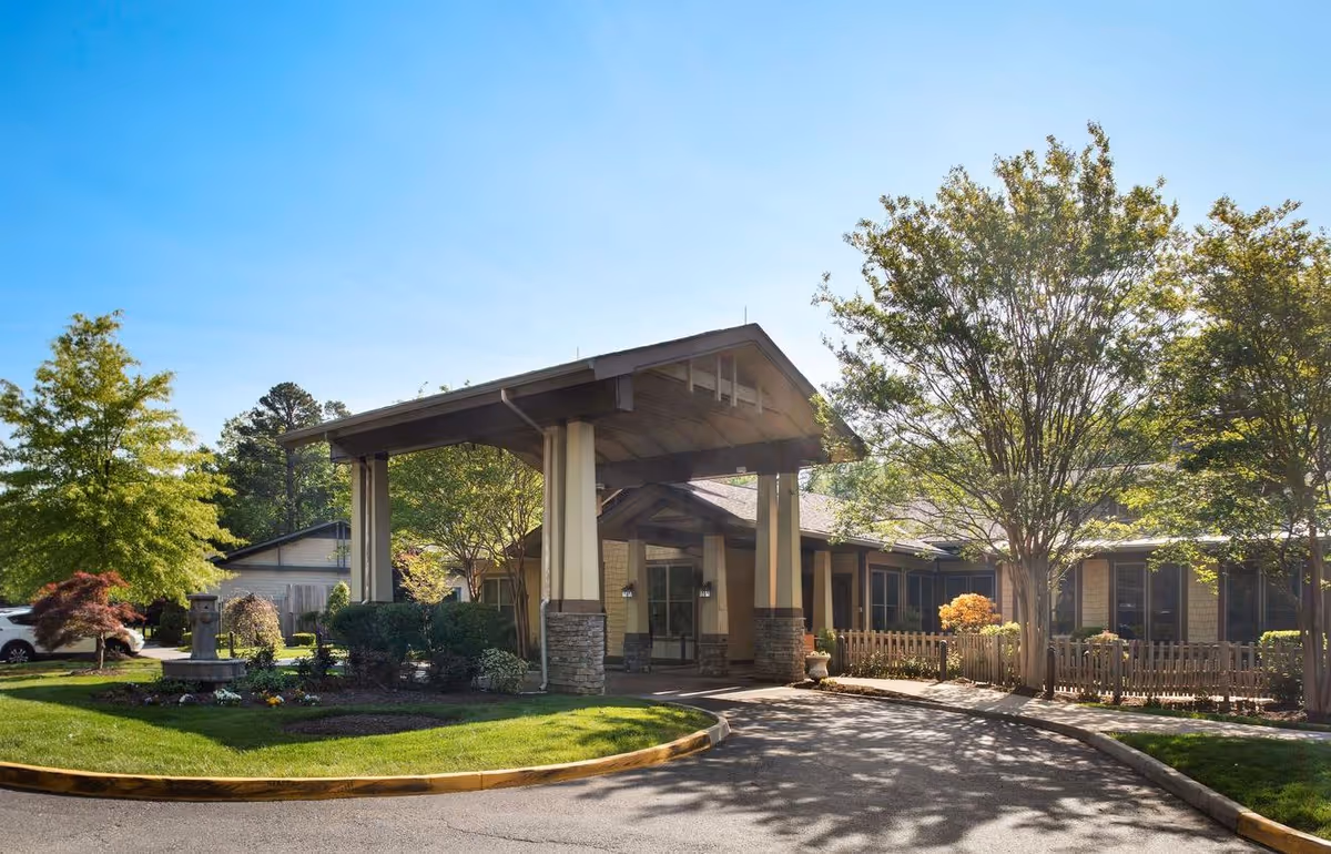 Covered entrance and porte-cochere of a senior living building surrounded by trees, landscaping, and a circular driveway.