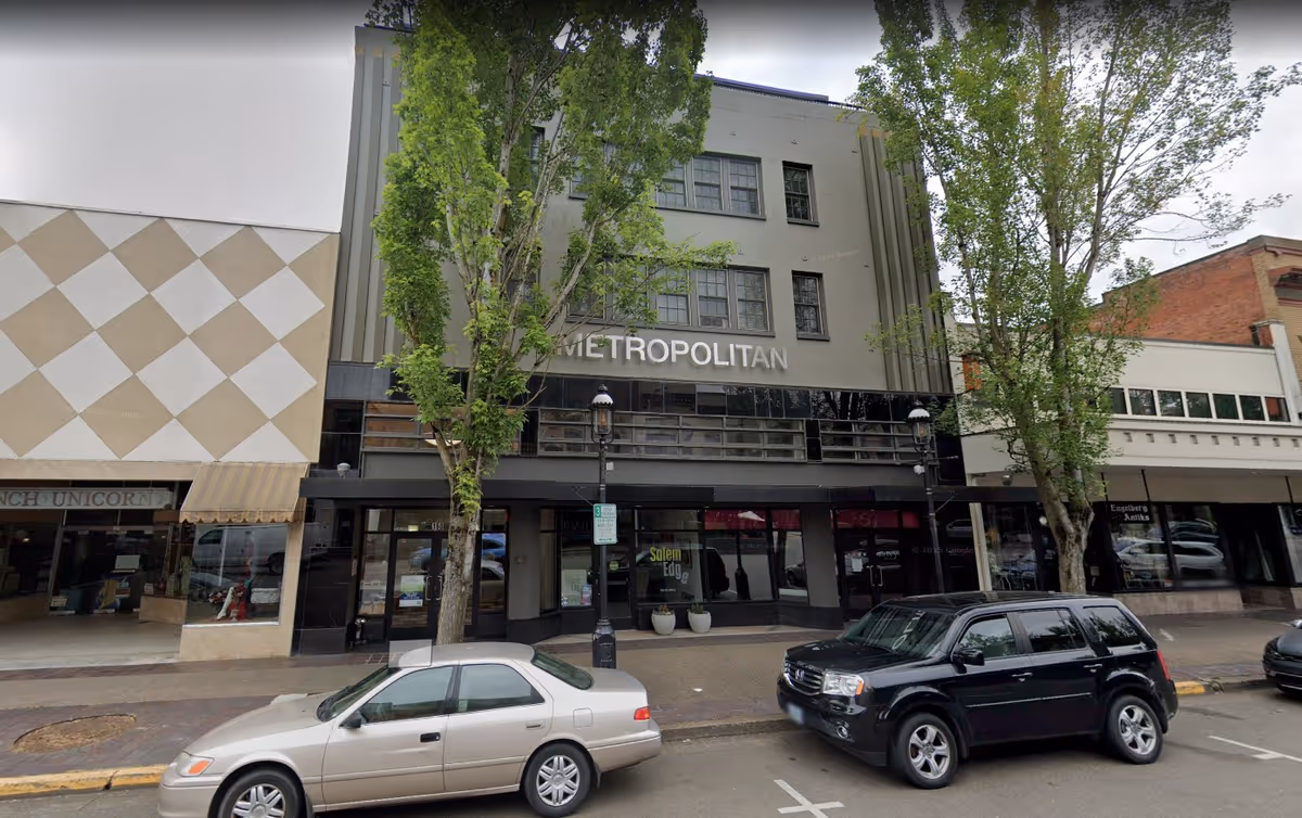 City street exterior of a storefront building named Metropolitan, with trees and parked cars.