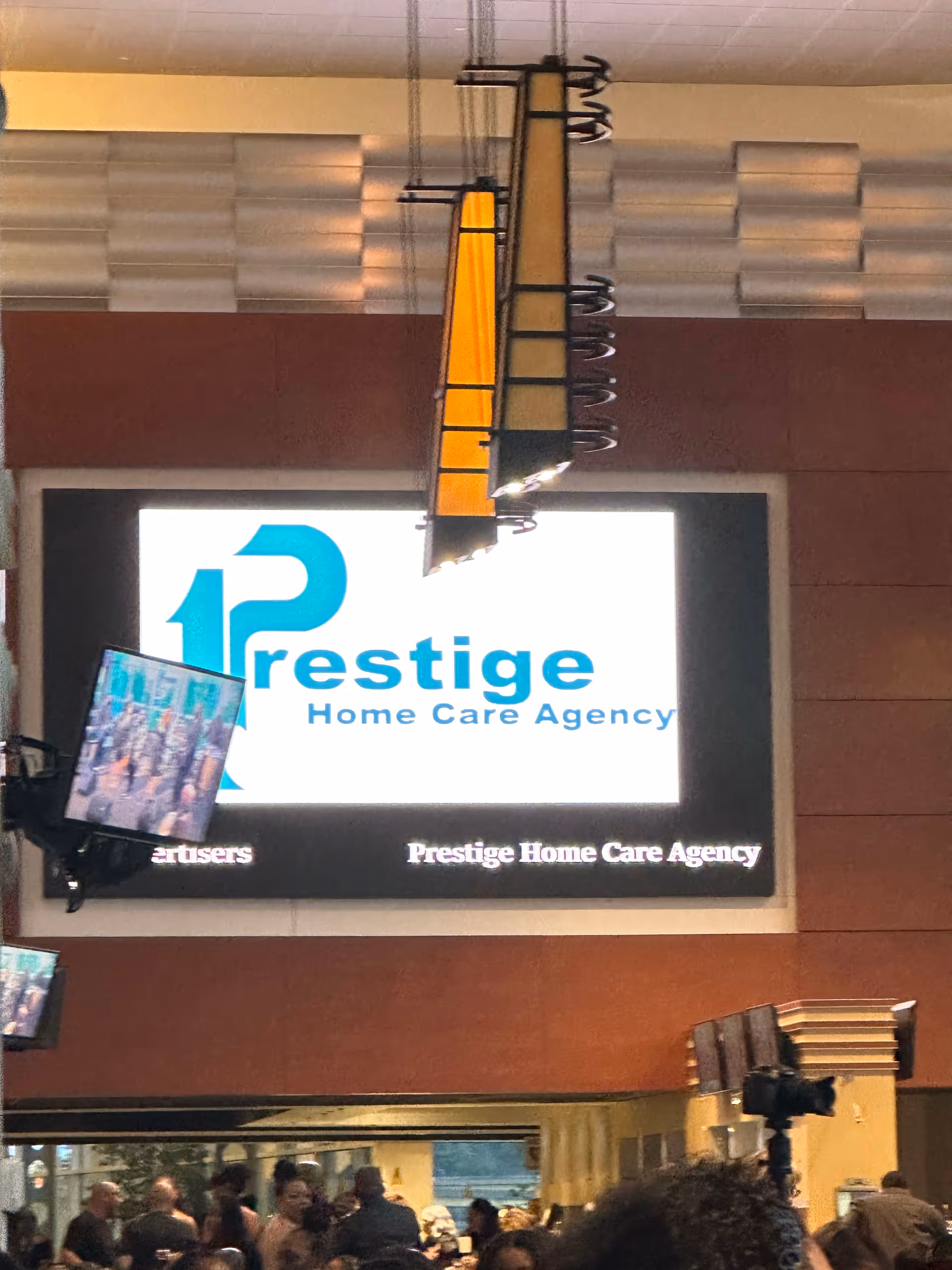 Indoor lobby with a large Prestige Home Care Agency sign and people in background.