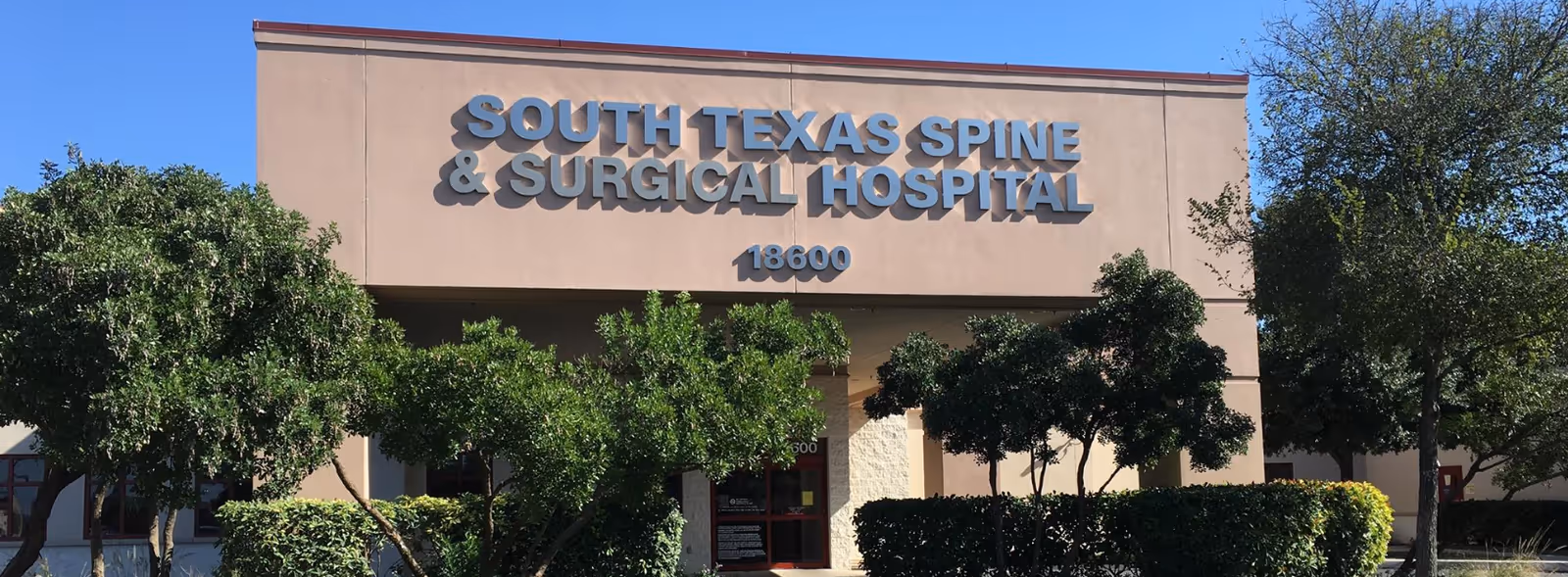Front view of South Texas Spine & Surgical Hospital with sign and trees.