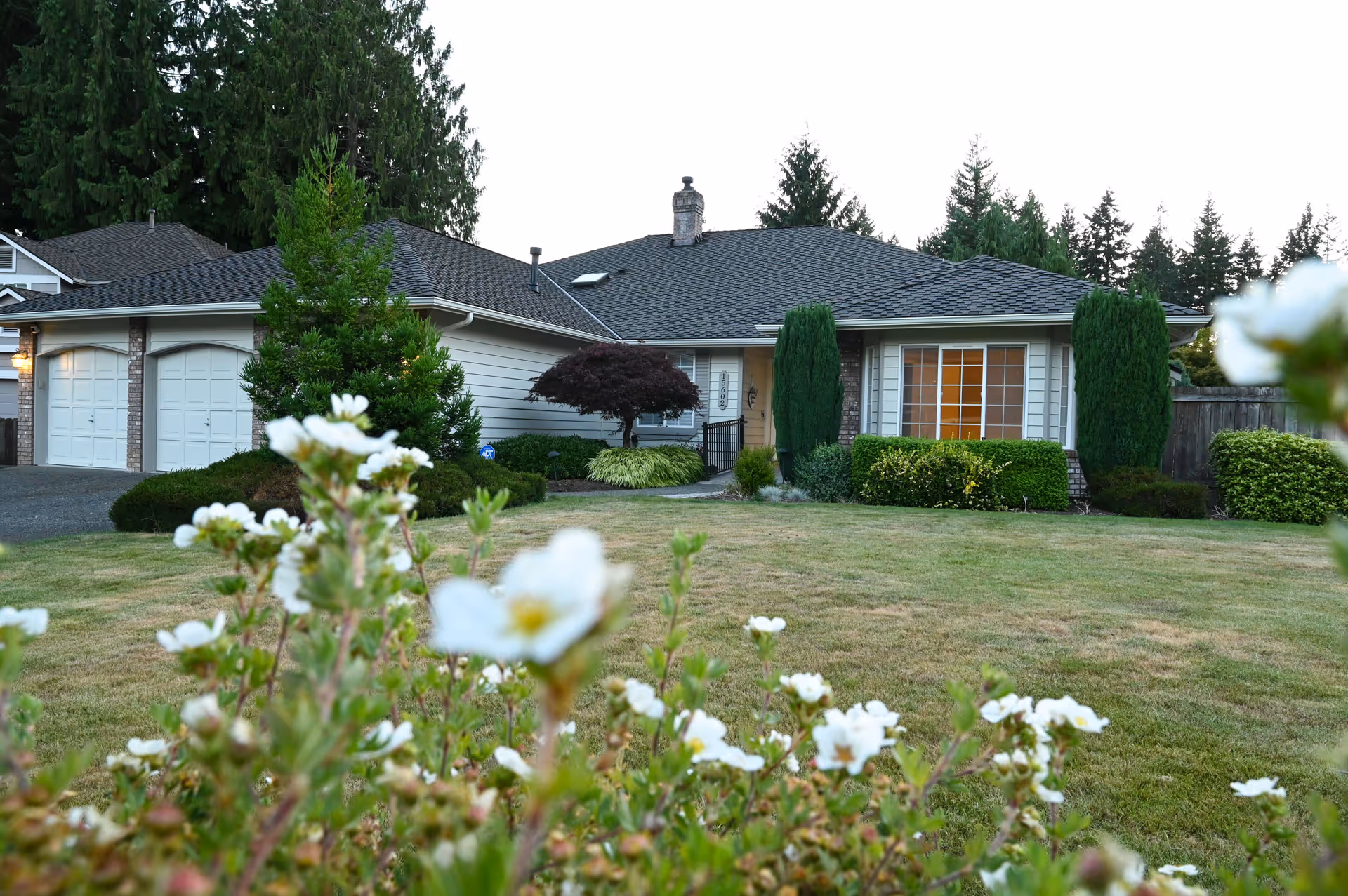 Front view of a single-story house with a two-car garage, manicured lawn, and shrubs