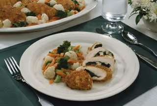 Plate of sliced chicken with vegetables on a formal dining table.