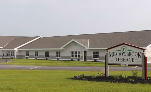Exterior view of Meadowbrook Terrace Assisted Living Facility with a sign in the foreground.